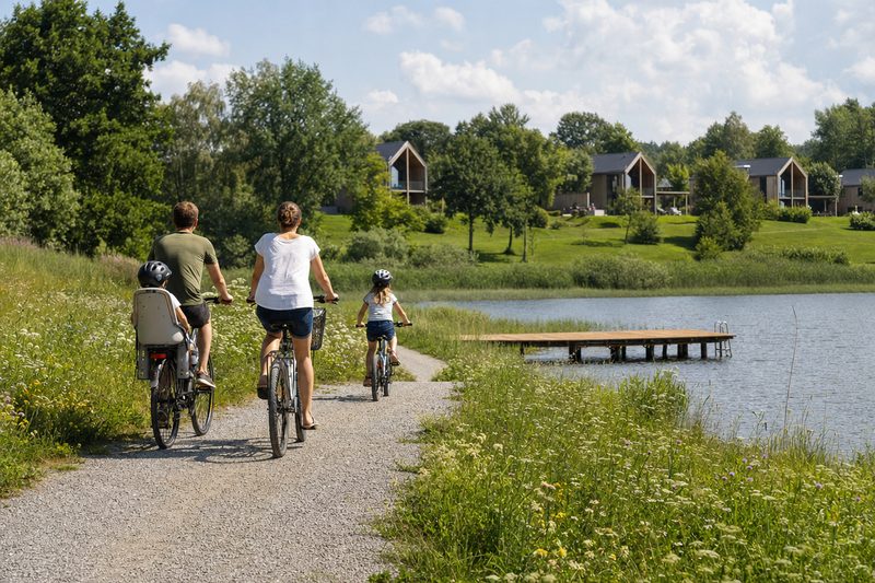 Familie auf Fahrradtour auf einem Uferweg an einem See im Frühsommer